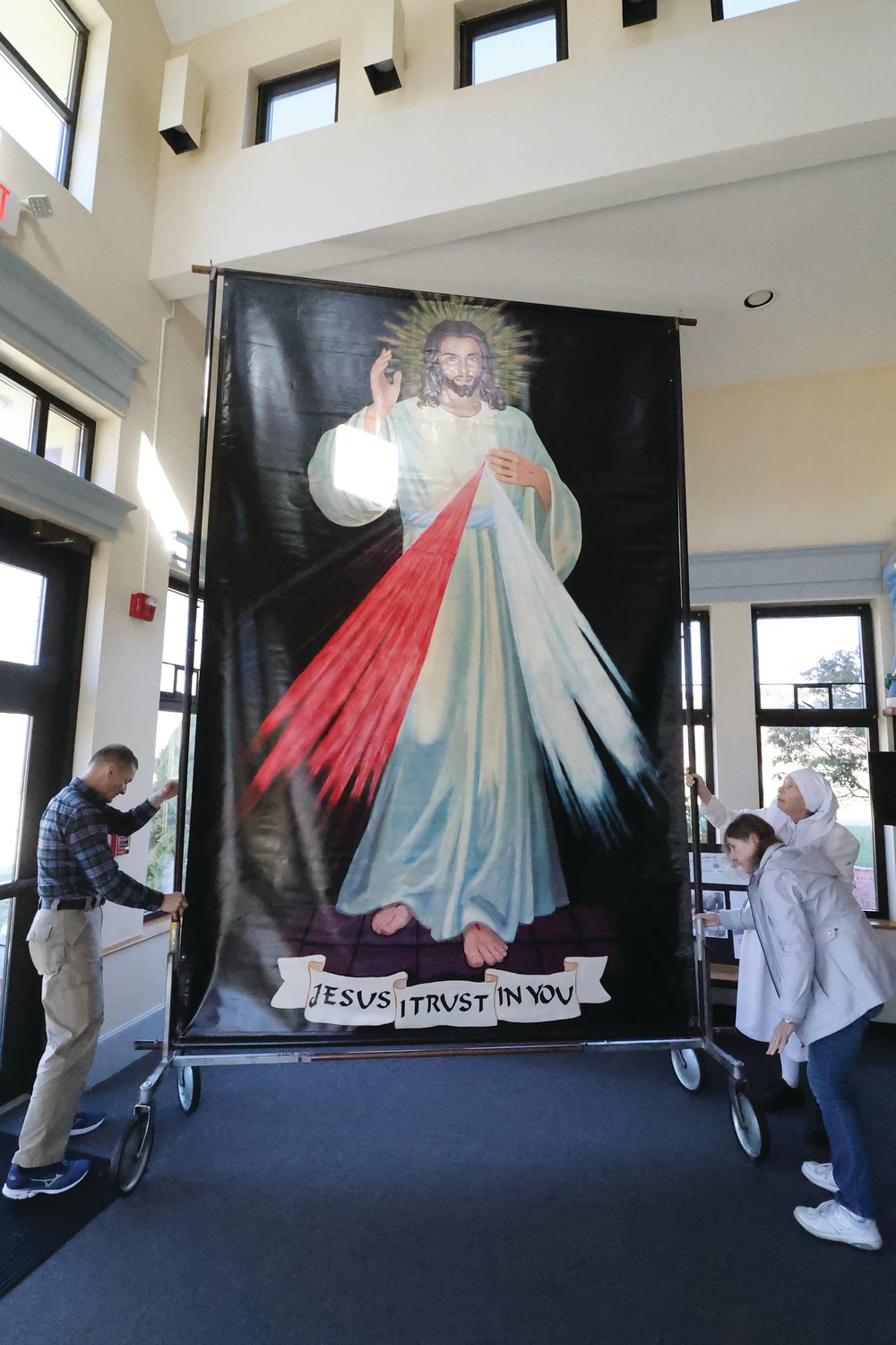 Marc Auger, Marie Magill and Sister Grace Coffey put into place at Saint Theresa Church, Nasonville, an image of Divine Mercy painted locally on a tarp nearly 30 years ago by Giselle McLear. Sister Grace helped to lead a pilgrimage of St. Patrick School students to the U.N. during a 1994 visit by then-Pope John Paul II, who saw and commented on the painting they brought.